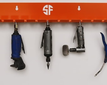 Puede incluir: Un soporte de herramientas de pared naranja con las letras "SF" en un círculo blanco. Cinco herramientas cuelgan del soporte, incluyendo una herramienta neumática azul, una herramienta neumática gris, una herramienta neumática gris con cabeza redonda y una herramienta neumática azul con mango curvo.