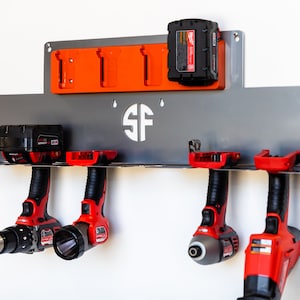May include: A metal wall-mounted organizer for power tools, featuring a gray metal base with a shelf, orange battery holders, and slots for four power tools. The organizer has a monogrammed "SF" in the center.