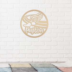 Puede incluir: Decoraci&oacute;n de pared circular de madera con un dise&ntilde;o recortado. El dise&ntilde;o presenta un emblema alado con el nombre "Peyton" en escritura cursiva. La decoraci&oacute;n de pared est&aacute; montada en una pared de ladrillo blanco.