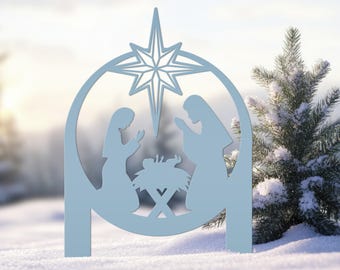 May include: A light blue, flat, circular metal cutout featuring a silhouette of a nativity scene. The design includes a large star at the top, with two figures kneeling on either side of a central manger containing a small infant figure.