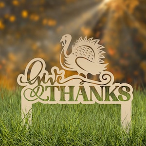 May include: A wooden Thanksgiving yard sign with the words "Give THANKS" and a turkey silhouette. The sign is light brown and is placed in green grass with a blurred autumn background.