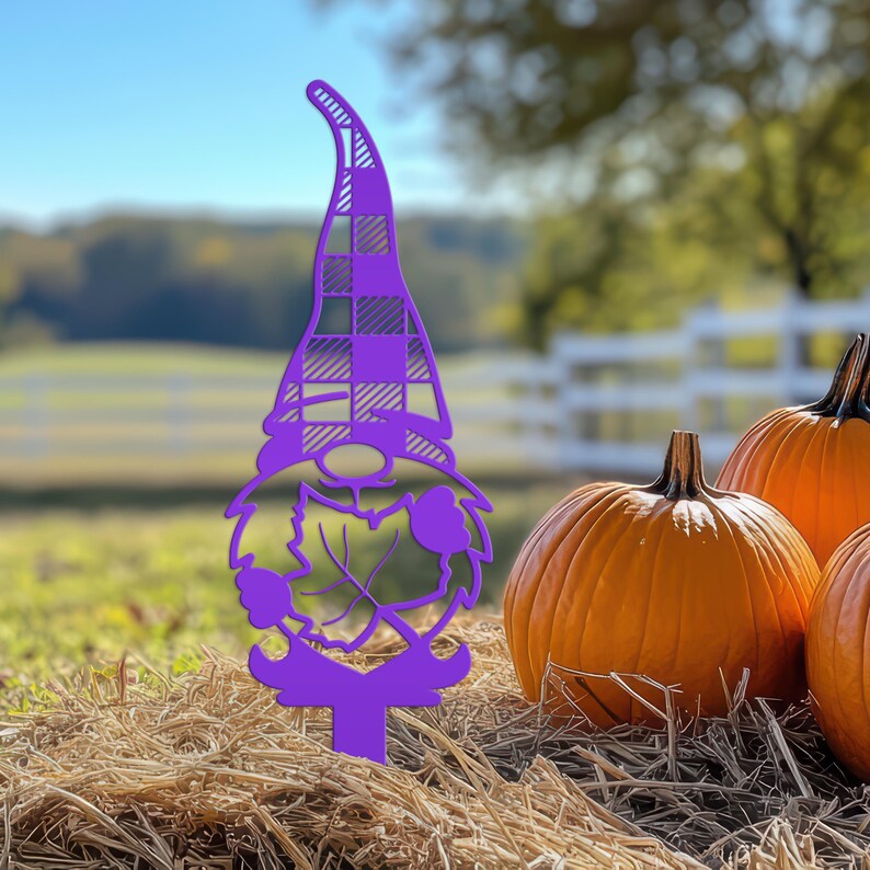 May include: A purple metal garden stake in the shape of a gnome, with a plaid pattern on the hat and a leaf design on the beard. The gnome is set in a hay bale with orange pumpkins in the background.