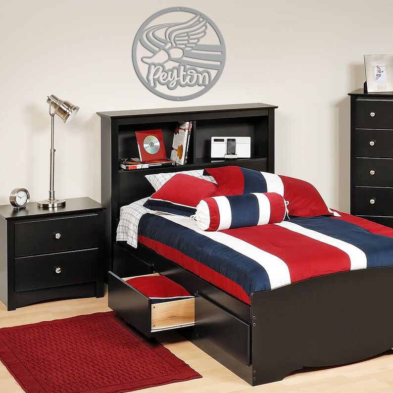 Puede incluir: Un juego de dormitorio con una estructura de cama negra, una mesita de noche y una c&oacute;moda. La cama tiene una colcha y almohadas a rayas rojas, blancas y azules. Una alfombra roja est&aacute; en el suelo. Decoraci&oacute;n de pared plateada con el nombre "Peyton".