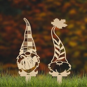 May include: Two wooden gnome yard stakes. One gnome has a plaid hat and a pumpkin, the other has a leaf-shaped hat. Both have beards and are on stakes for easy placement in the yard.