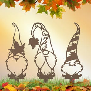 May include: Three brown metal garden gnomes with leaf accents. Each gnome has a different hat design, with one featuring a maple leaf. The gnomes are placed in a grassy area with autumn leaves and a blurred background.