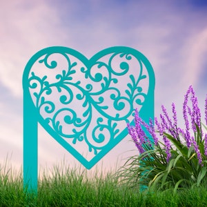 May include: A teal blue metal heart-shaped garden stake with a decorative filigree design. The stake is in front of a purple flower bush and a green grassy field.