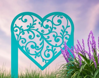 May include: A teal blue metal heart-shaped garden stake with a decorative filigree design. The stake is in front of a purple flower bush and a green grassy field.