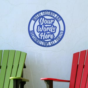 May include: A blue circular wall sign with the text "Where Friends and Your Words Here Marshmallows Get Toasted". Two Adirondack chairs, one green and one red, are in the foreground.