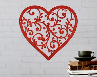 May include: Red metal heart-shaped wall decor with a decorative filigree design. The heart is hanging on a white brick wall.