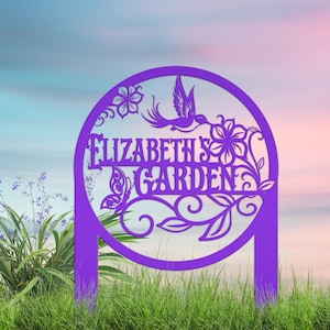 May include: A circular purple garden stake featuring a cutout design of a hummingbird, a butterfly, and floral motifs. The text "ELIZABETH'S GARDEN" is prominently displayed in the center of the circle, supported by two vertical stakes.