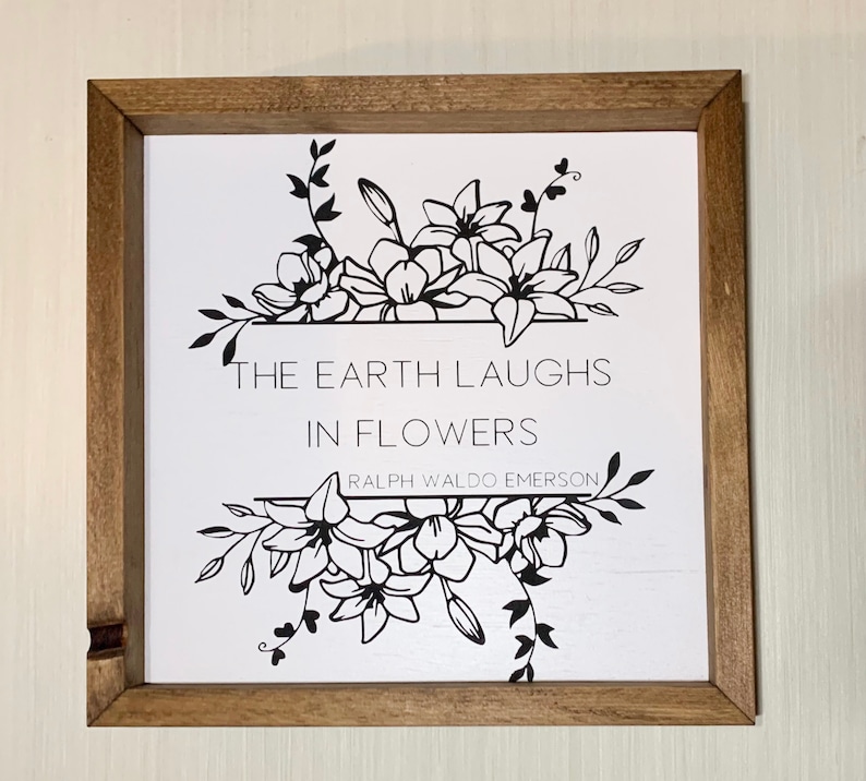 Puede incluir: Una impresi&oacute;n enmarcada en blanco y negro con un dise&ntilde;o floral y la cita "La tierra se r&iacute;e en flores" de Ralph Waldo Emerson.