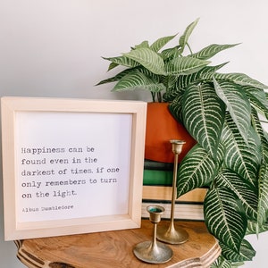 May include: A framed print with a white background and black text. The quote reads "Happiness can be found even in the darkest of times, if one only remembers to turn on the light." The quote is attributed to Albus Dumbledore.