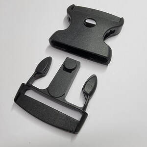 May include: Black plastic buckle with two separate pieces. The buckle is designed to be used with webbing or straps.