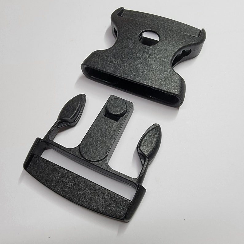 May include: Black plastic buckle with two separate pieces. The buckle is designed to be used with webbing or straps.