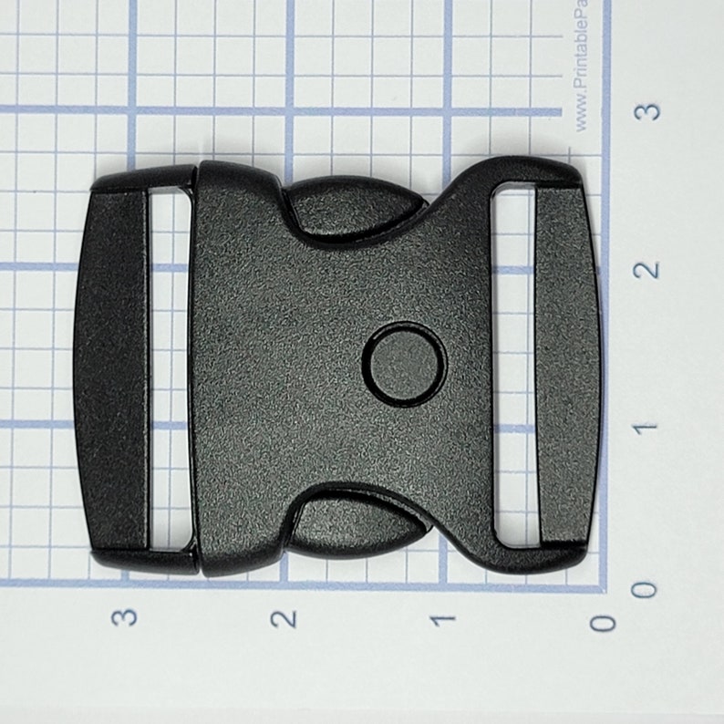 May include: Black plastic side release buckle. The buckle is approximately 5 cm long and 2.5 cm wide.