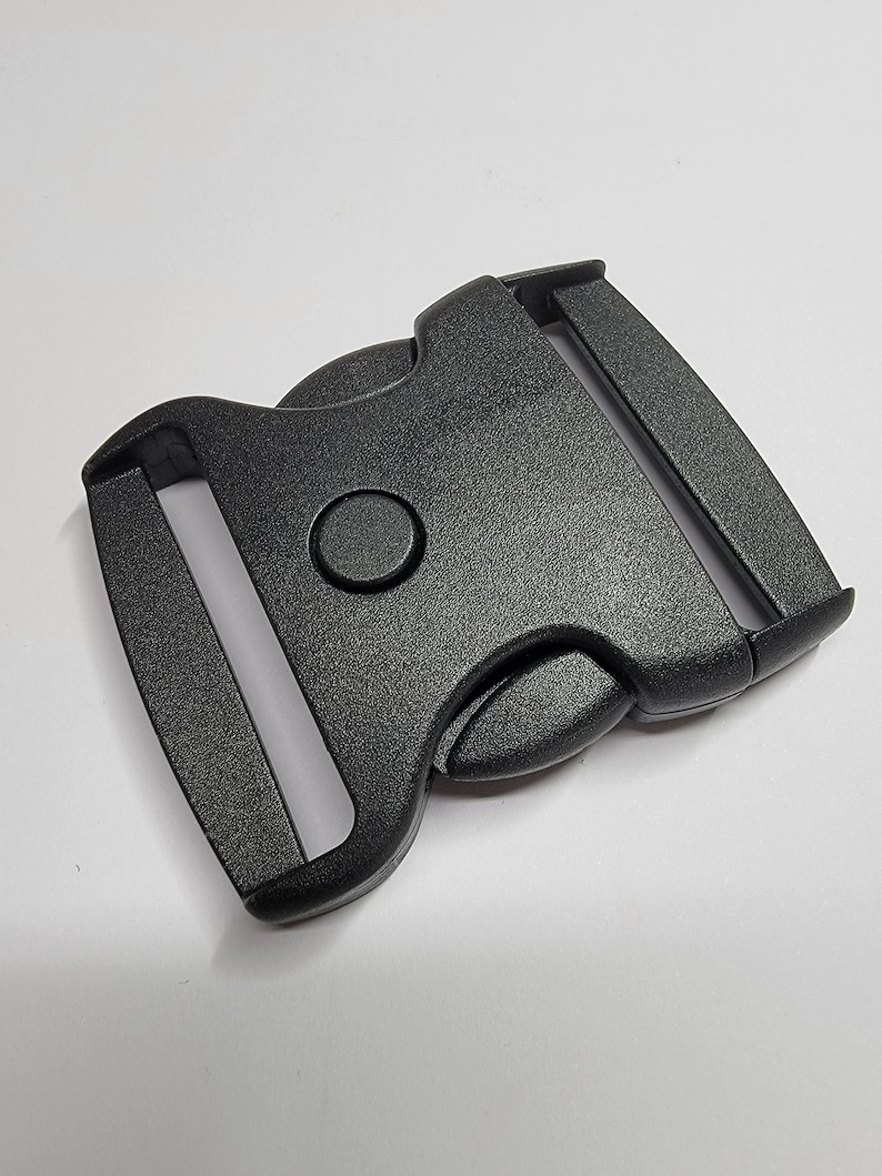 May include: A black plastic buckle with a side release mechanism. The buckle is designed for use with webbing or straps.