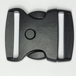 May include: Black plastic side release buckle. The buckle has a smooth, matte finish and a rounded shape.