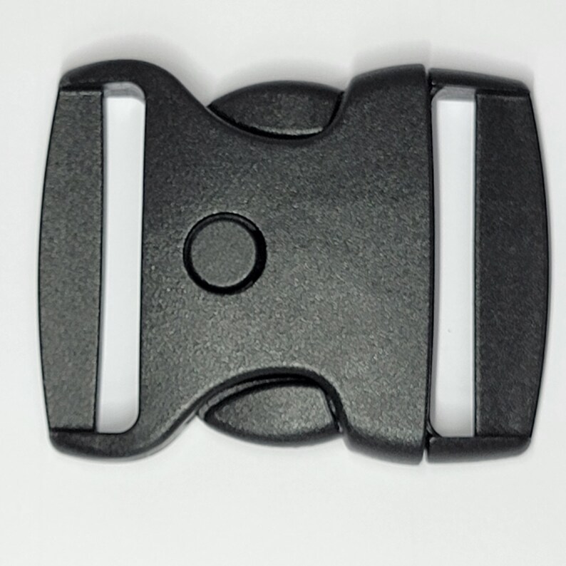 May include: Black plastic side release buckle. The buckle has a smooth, matte finish and a rounded shape.