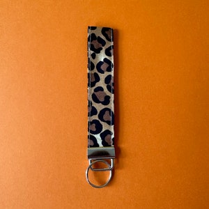 May include: A brown and black leopard print key chain with a silver key ring.
