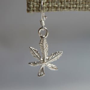 Puede incluir: Pendientes de plata con un diseño detallado de hoja de marihuana.