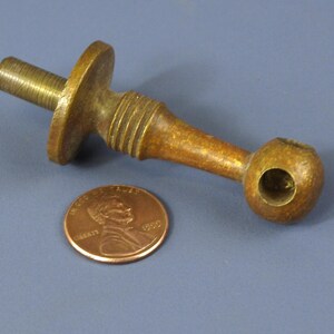 May include: A vintage brass hardware piece with a threaded end, a circular flange, and a rounded end with a hole. A penny is next to the hardware for size comparison. The hardware is a warm, aged brass color.