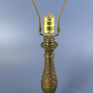 Puede incluir: Una lámpara de mesa de latón con una base decorativa texturizada y un soporte curvo para la pantalla. La lámpara tiene un diseño detallado y estampado en la columna central y una base redonda. La lámpara mide aproximadamente 46 cm de alto.