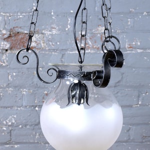 May include: A vintage hanging lamp with a frosted glass globe and ornate black metal accents. The lamp is suspended by chains and features decorative scrollwork. The design is reminiscent of antique lighting fixtures.