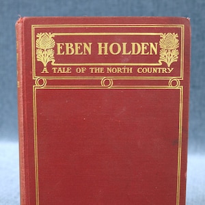 Puede incluir: Un libro de tapa dura rojo con letras doradas en la portada. El título es "Eben Holden: A Tale of the North Country" de Irving Bacheller.