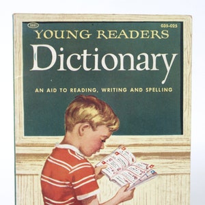 May include: A vintage children's book cover for a "Young Readers Dictionary." The illustration shows a young person reading the dictionary, wearing a red and white striped top and blue trousers. The book is described as an aid to reading, writing, and spelling.