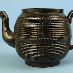 May include: A black ceramic teapot with a textured, ribbed design. The teapot has a rounded body and a spout on one side and a handle on the other.