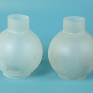 May include: Two spherical lamp shades made of frosted white glass. Each shade features a rounded, bulbous body that tapers into a cylindrical neck opening at the top. The glass has a semi-translucent, matte finish that diffuses light evenly.