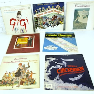 Puede incluir: Una colección de discos de vinilo vintage con portadas de álbumes con varios diseños y texto. Los títulos incluyen "Gigi", "The Night They Raided Minsky's", "Ryan's Daughter", "The Great Caruso", "Movie Themes", "Sweet Charity" y "The Best of Chickenman".