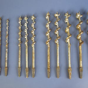May include: A collection of antique drill bits, varying in size and design. The bits are made of metal with a golden hue and show signs of age and use. The spiral flutes and pointed tips are clearly visible, suggesting their use in woodworking or construction.