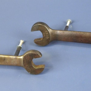 Può includere: Due chiavi inglesi antiche in bronzo con estremità aperte, ciascuna con un piccolo piolo bianco attaccato. Le chiavi sono su uno sfondo blu. Una chiave ha il numero "2121" stampigliato.