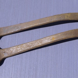 May include: Two rusty wrenches with a curved handle. The wrenches have a hexagonal opening on one end and a rounded opening on the other end.