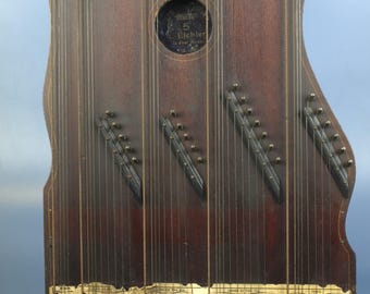 May include: A vintage Regent Zither, a stringed musical instrument, with a dark wood finish. The instrument features numerous strings, tuning pegs, and a sound hole. A gold label at the bottom reads "Regent Zither No. 5".