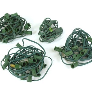 May include: Four tangled sets of green Christmas light strings with empty sockets and green cords. The cords have a standard two-prong plug. The lights are on a white background.