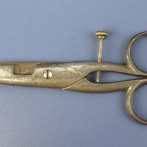 Può includere: Forbici antiche in metallo con una lama appuntita e due anelli per le dita. Le forbici hanno una vite al centro e una finitura color ottone. Probabilmente utilizzate per cucire o creare.
