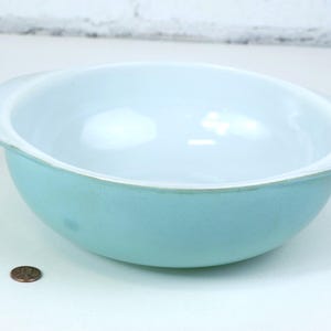 May include: A light blue Pyrex mixing bowl with white interior and two handles. The bowl is on a white surface.
