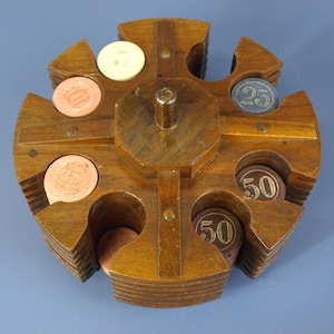 May include: A circular wooden carousel chip holder with a central handle, featuring eight slots containing stacks of round gaming chips. The chips are in various colors including cream, peach, dark blue, and brown, with numerical values 5, 25, and 50.