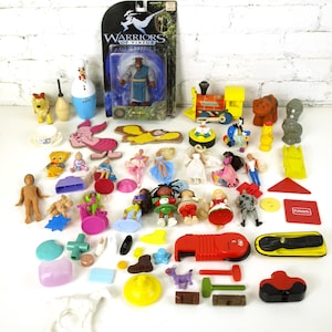 May include: A collection of various toys and figurines, including a train, a doll, a pig, a snowman, a dog, a figure in a blue robe, and a variety of other plastic toys.