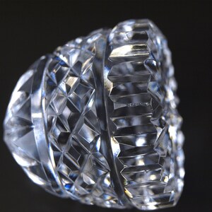 May include: A clear, cut-glass object with a geometric pattern. The object has a diamond-like design and a ridged edge. The facets catch the light, creating a sparkling effect. The object is likely a decorative piece or part of a glassware set.