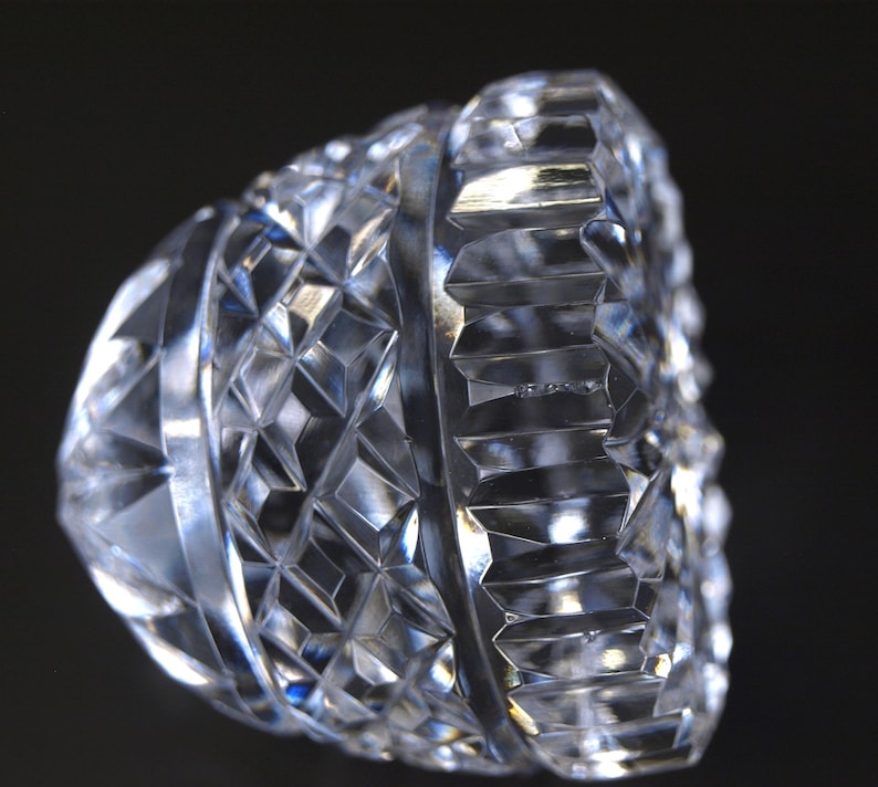 May include: A clear, cut-glass object with a geometric pattern. The object has a diamond-like design and a ridged edge. The facets catch the light, creating a sparkling effect. The object is likely a decorative piece or part of a glassware set.