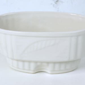 May include: Off-white ceramic planter with a leaf design. The oval-shaped planter has a ribbed exterior and a stepped base. A decorative piece for indoor plants.
