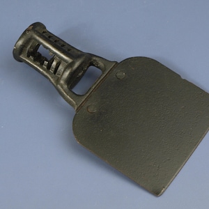 May include: Black cast iron stove top grate with a raised, open-sided, rectangular base. The grate is designed to hold a small pot or pan over a stovetop burner.