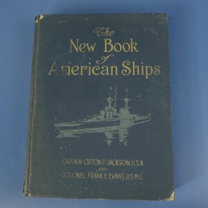 May include: A vintage book titled "The New Book of American Ships" with gold lettering and an illustration of a ship. The cover is a dark blue color. The authors are Captain Orton P. Jackson, U.S.N. and Colonel Frank E. Evans, U.S.M.C.
