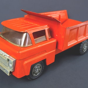 May include: A vintage, bright orange toy dump truck with a silver-colored front grill and clear windshield. The truck has black tires and a detailed dump bed. A classic toy for children.