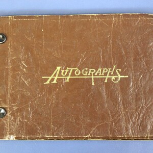 May include: A brown autograph book with the word "AUTOGRAPHS" in gold lettering. The cover has a textured appearance and is held together with two silver rivets.