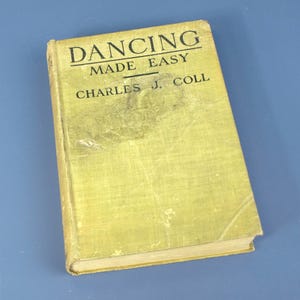 Puede incluir: Un libro antiguo titulado "DANCING MADE EASY" de Charles J. Coll. La portada es de color verde pálido descolorido con texto negro. El libro muestra signos de edad, con desgaste y decoloración visibles en la portada.