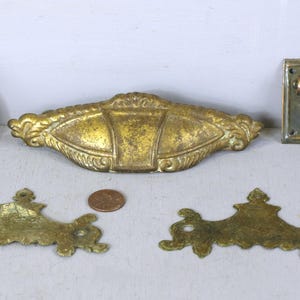 May include: Five antique brass drawer pulls, including a ring pull, a rectangular pull with a curved handle, and two ornate pulls with a decorative design.